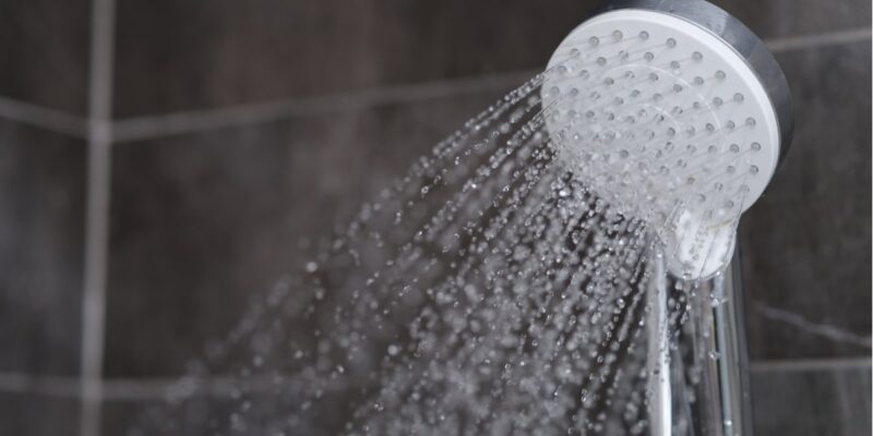 Eine Duschbrause, aus welcher Wasser kommt und Wasserdampf entweicht, in den Aerosolen können sich Legionellen befinden, die für den Menschen gefährlich sind