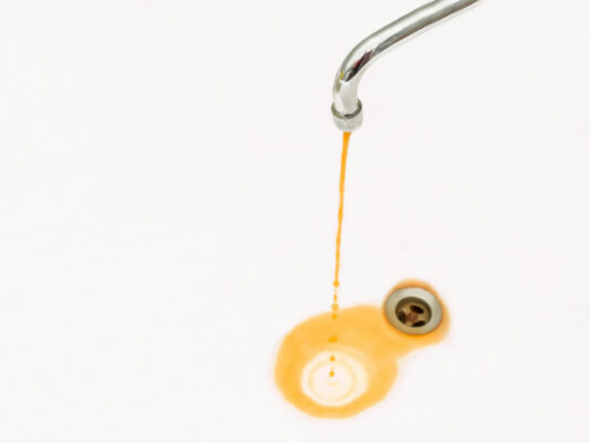 Das Bild zeigt einen Wasserhahn aus dem braunes, rostiges Wasser in ein weißes Waschbecken fließt. Das Wasser bildet einen bräunlichen Fleck, während es in den Abfluss läuft.